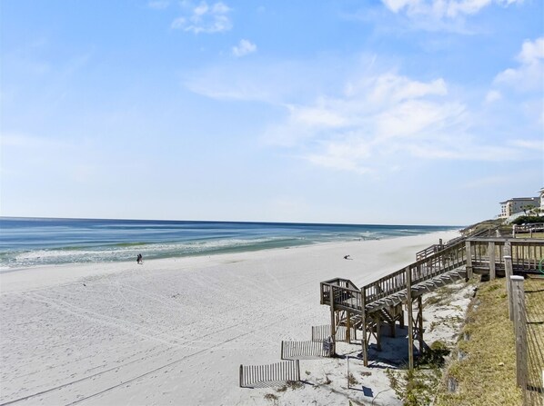 Walk along the boardwalk to the wide, open beach with a gentle slope leading to the water.