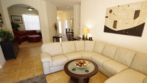 A living room with a beige sectional sofa, a round coffee table with a bowl of snacks, and a painting on the wall. - Ly231617 - Watersong - 6 Bed 4 Baths Villa (Davenport)