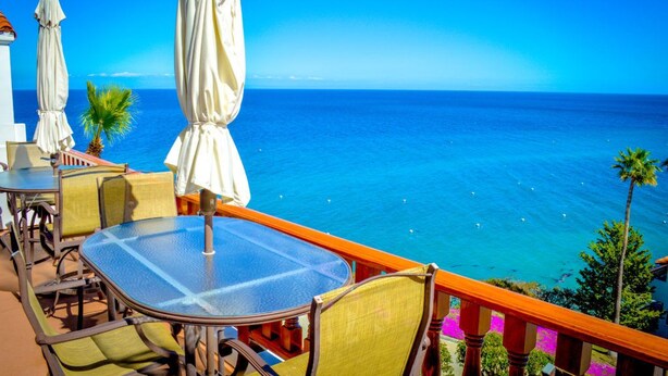 Un balcón con mesa y sillas de vidrio, con vista a un mar azul y transparente.