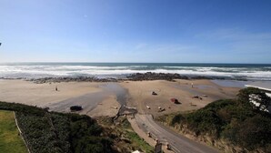 Una playa con costa rocosa, un camino que lleva a la playa y un cielo azul despejado.