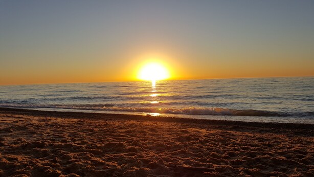 Una playa al atardecer, con el sol reflejado en el agua.