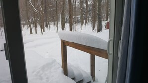 Escena nevada al aire libre con un banco de madera cubierto de nieve, visible a través de una ventana.