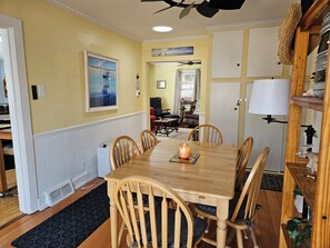 A dining area with a wooden table and chairs, a candle on the table, and a view into the living room.
