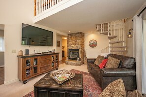 A living room with a stone fireplace, leather sofa, and a flat-screen TV.