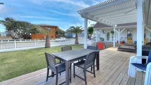 Une terrasse extérieure couverte, dotée d’une table et de chaises, d’une clôture blanche et offrant une vue sur un quartier résidentiel avec des maisons et des arbres.