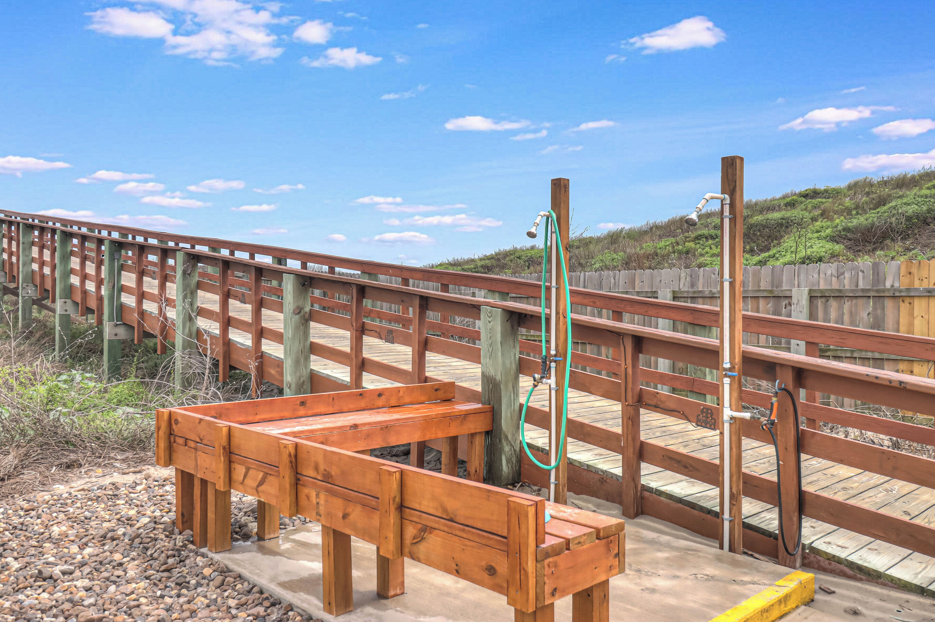 A wooden deck with a bench, a hose, and a wooden fence.