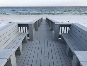 A wooden pier leading to a beach with benches.