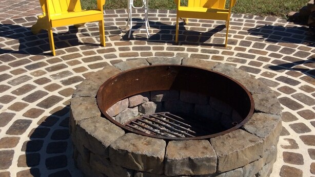 A circular stone fire pit with two yellow Adirondack chairs and a small round table. - Country Living with a Twist (Bolivia)