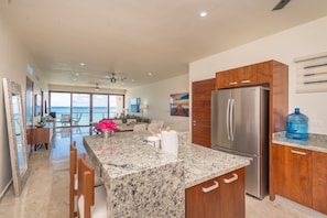 A spacious kitchen with a large island, stainless steel appliances, and a view to the outside.