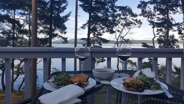 A table set with food and wine glasses overlooking a lake with trees and mountains in the background.