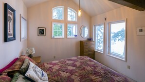 A bedroom with a bed, dresser, and multiple windows.