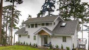 A two-story house with a porch, a deck, and a view of the water.