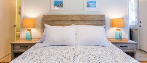 A bedroom with a wooden headboard, two white pillows, a patterned bedspread, and two bedside tables with lamps.