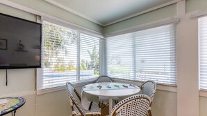 Ein Eckzimmer mit rundem Tisch und vier Stühlen, großen Fenstern mit Jalousien und einem flachbildfernseher an der Wand.