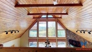 Una habitación con techo de madera inclinado, ventanas amplias y pared de piedra.
