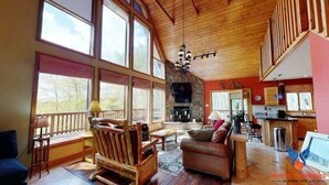 Amplia sala de estar con ventanas grandes, chimenea y zona de cocina.