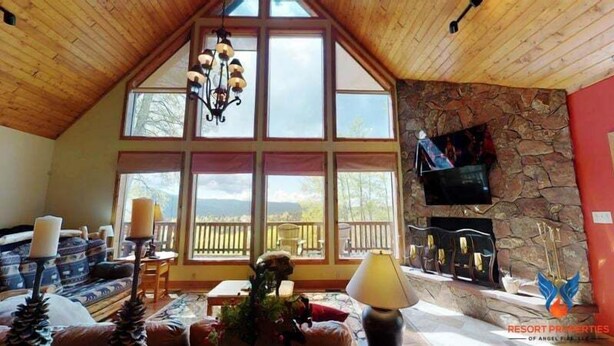 Una sala de estar acogedora con chimenea de piedra, ventanas amplias y techo de madera.