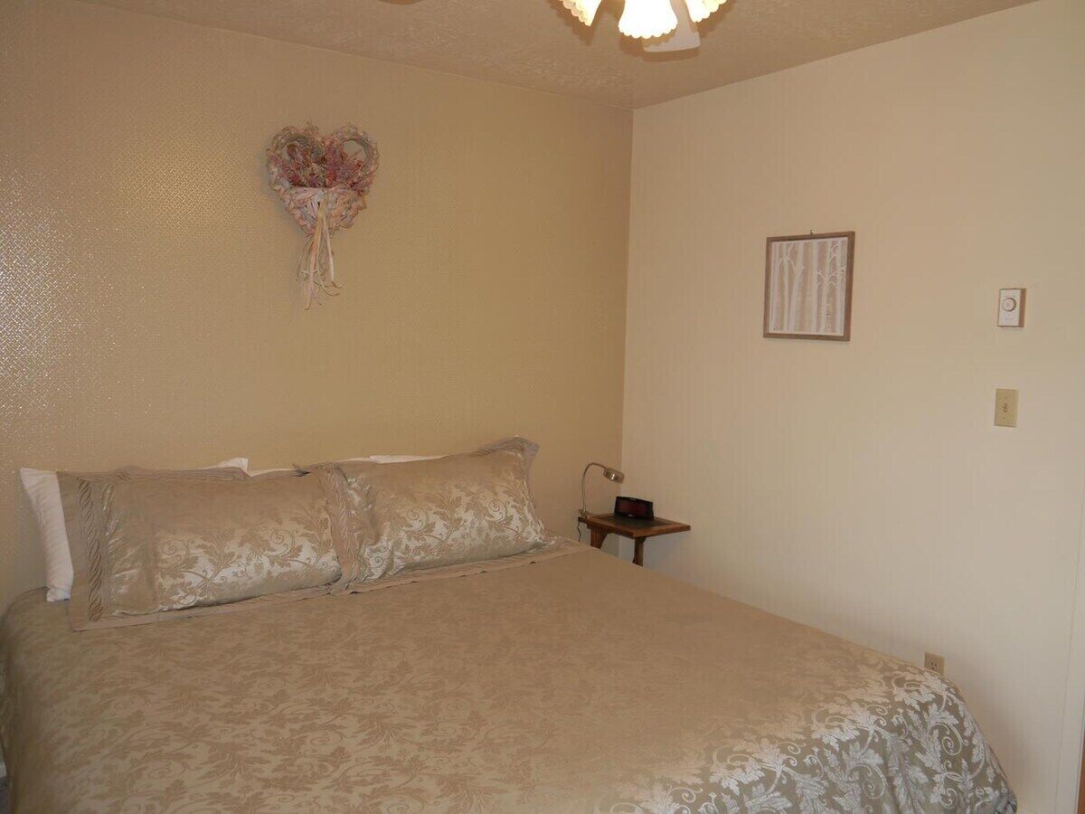 A bedroom with a bed, a nightstand, a wall-mounted lamp, and a framed picture.