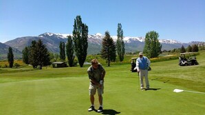 A golf course with a mountainous backdrop, a golf cart, and a person preparing to putt.