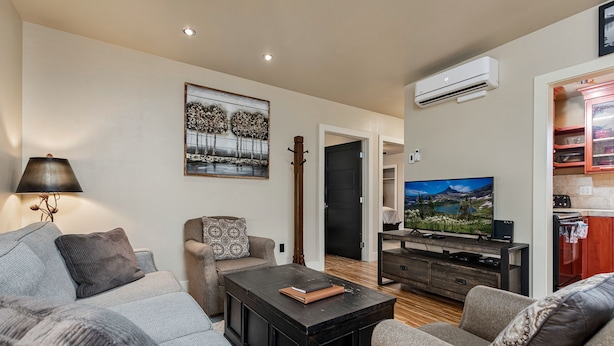 Un salon moderne avec un canapé, une table basse et un téléviseur. Un tableau est accroché au mur et un appareil de climatisation est placé au-dessus du téléviseur.