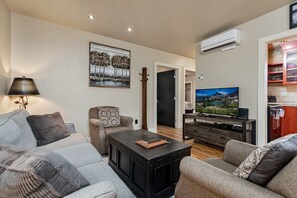 Un salon moderne avec un canapé, une table basse et un téléviseur. Un tableau est accroché au mur et un appareil de climatisation est placé au-dessus du téléviseur.