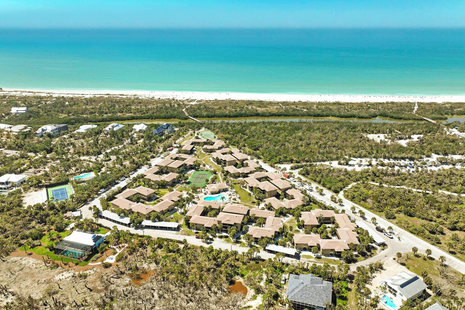 An aerial view of a resort with multiple buildings, a tennis court, and a beach.