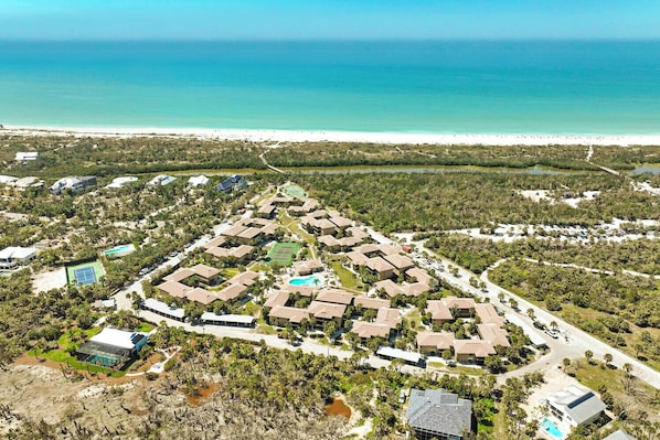 An aerial view of a resort with multiple buildings, a tennis court, and a beach.