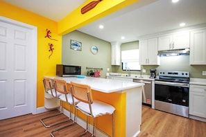 A modern kitchen with a central island, white cabinets, a microwave, a stove, and a sink.