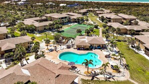 Un resort con piscina central, varias construcciones y vista a la playa.