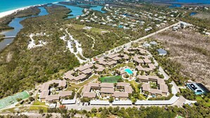 Vista aérea de un complejo turístico con varias edificaciones, cancha de tenis y piscina.
