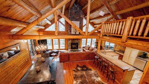 Un intérieur spacieux de chalet en bois, comprenant un coin repas, un espace salon, une cuisine et une cheminée.