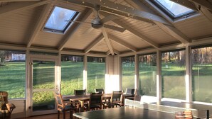 Un solárium con mesa de ping pong, ventanas amplias y vistas a un campo verde.