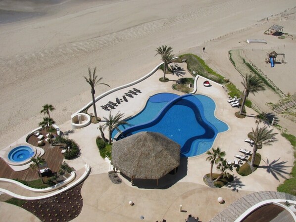 Um resort com uma piscina grande, palmeiras e uma área de praia.