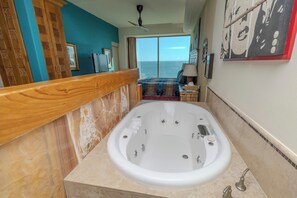A spacious bathroom with a large bathtub, a wooden vanity, and a view of the ocean.