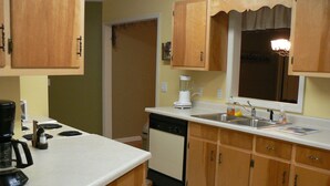 Una cocina compacta con armarios de madera, lavavajillas integrado y encimera blanca.