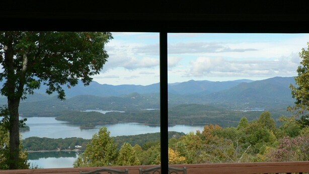 Vista desde un balcón con mesa y sillas, con vistas a un lago y montañas.