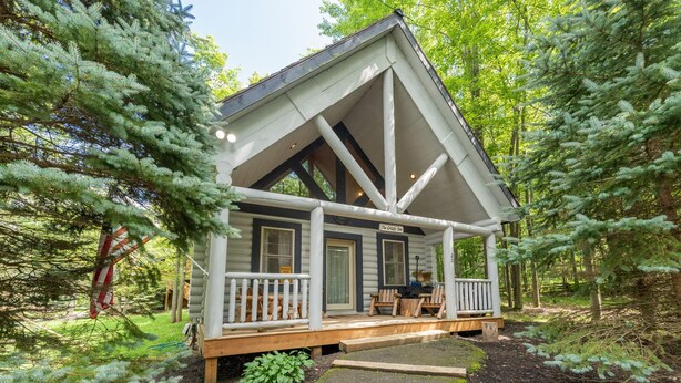 A cabin with a porch, surrounded by trees.