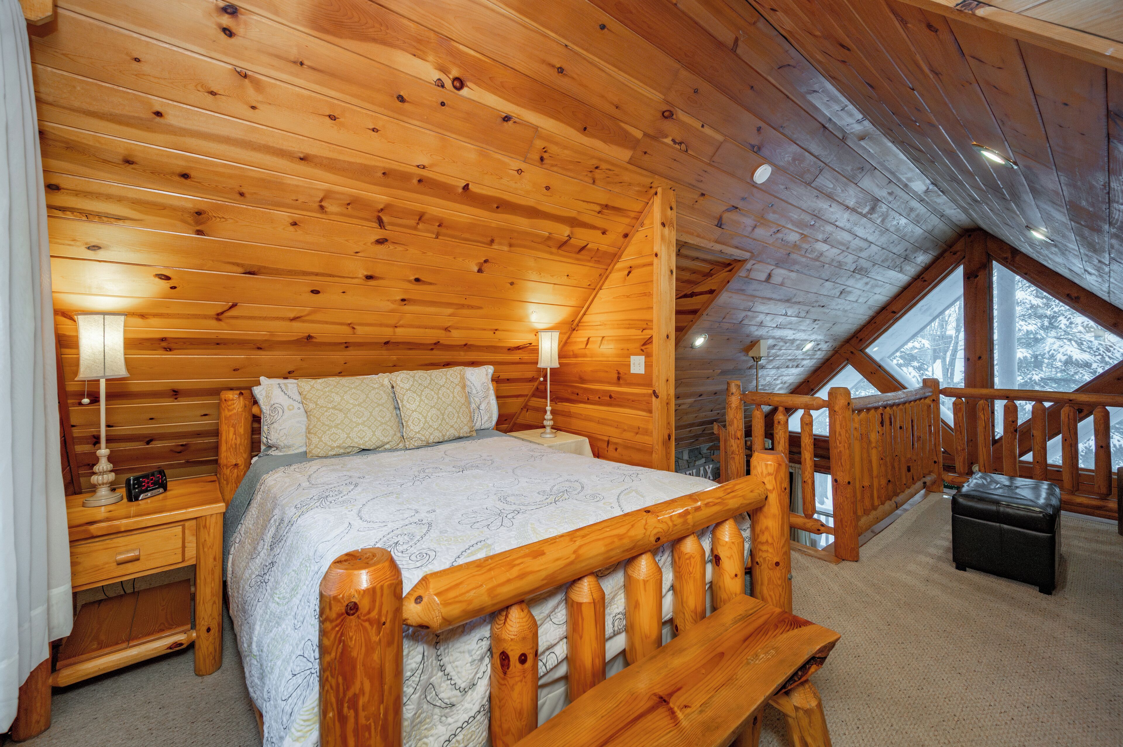 Un dormitorio de cabaña de madera con cama, mesitas de noche y una pequeña mesa.