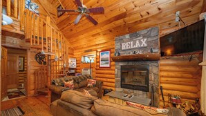 A cozy log cabin interior with a fireplace, a sofa, and a ceiling fan.