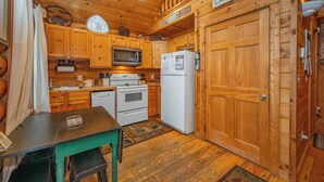 A wooden cabin kitchen with a microwave, refrigerator, stove, and wooden cabinets.