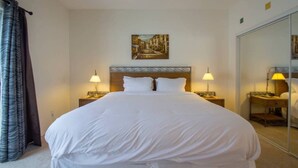 Habitación de hotel con una cama grande, dos lámparas de noche, un cuadro en la pared y un espejo en la pared opuesta.