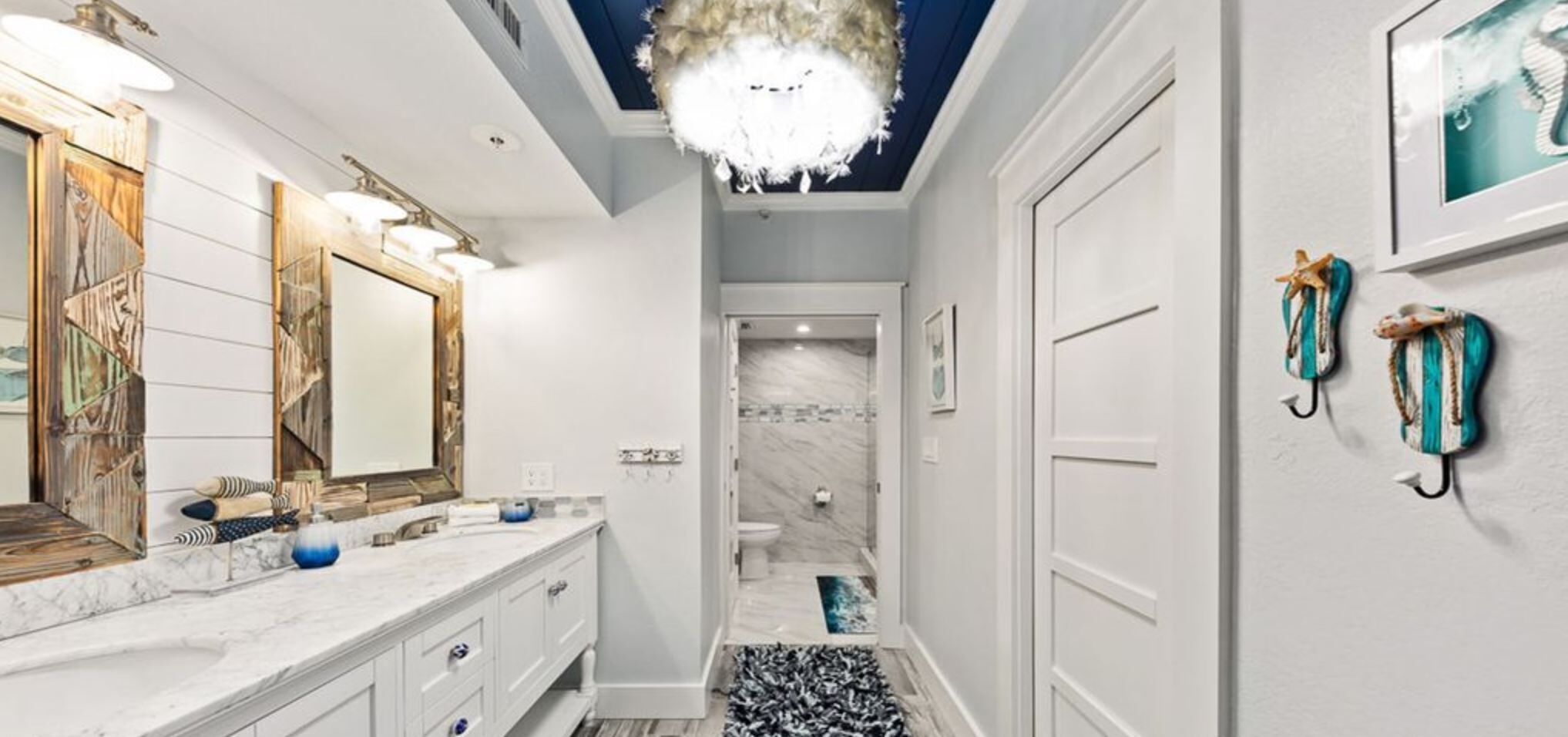 A modern bathroom with a marble shower, a chandelier, and a nautical-themed wall decoration.