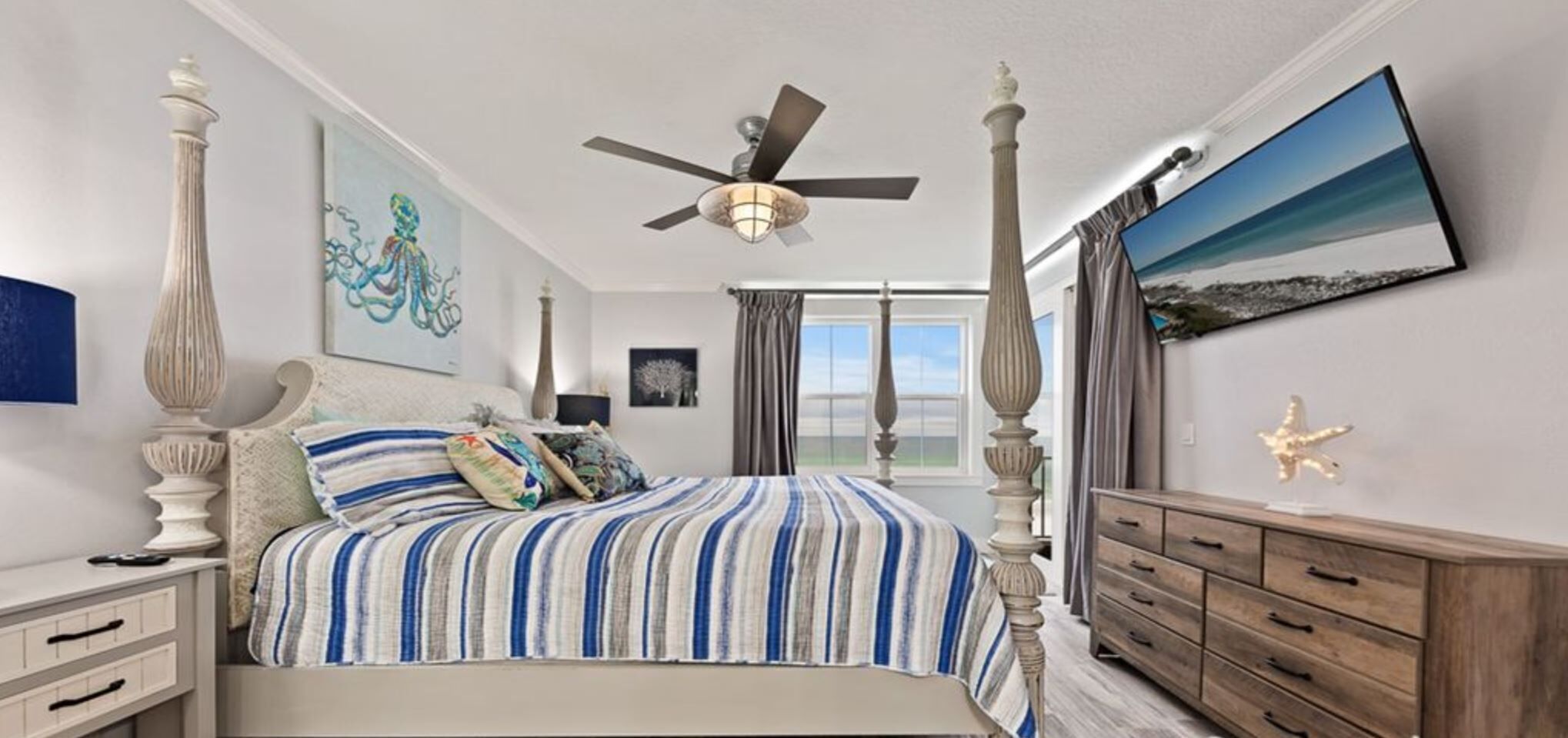 Une chambre à coucher avec un lit à baldaquin, un ventilateur de plafond, une grande fenêtre avec des rideaux et une vue sur l’extérieur.