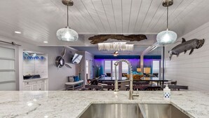 Una cocina moderna con una isla grande, luces colgantes y detalles decorativos en la pared.