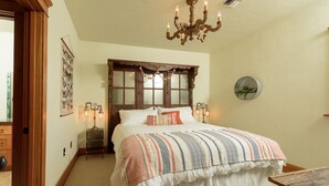 Quarto com uma cama grande, cabeceira de madeira, candelabro e mesa de cabeceira com uma luminária.