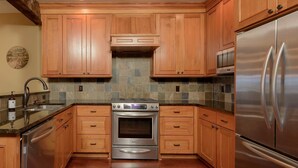 Uma cozinha com armários de madeira, geladeira de aço inoxidável, forno embutido e painel de azulejos.
