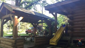 A wooden play area with a slide, benches, and a covered seating area.