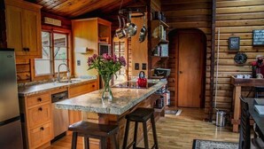 A rustic kitchen with wooden cabinets, a granite countertop, and a central island with stools. - ✨Rustic Cabin in Dry Creek Valley with beautiful views // 5 miles to Plaza ✨ (Healdsburg)