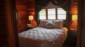 A wooden cabin bedroom with a bed, two bedside lamps, and a window with curtains. - ✨Rustic Cabin in Dry Creek Valley with beautiful views // 5 miles to Plaza ✨ (Healdsburg)
