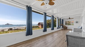 Una habitación amplia con ventanas grandes, piso de madera, ventiladores de techo y vista a la playa y al océano.
